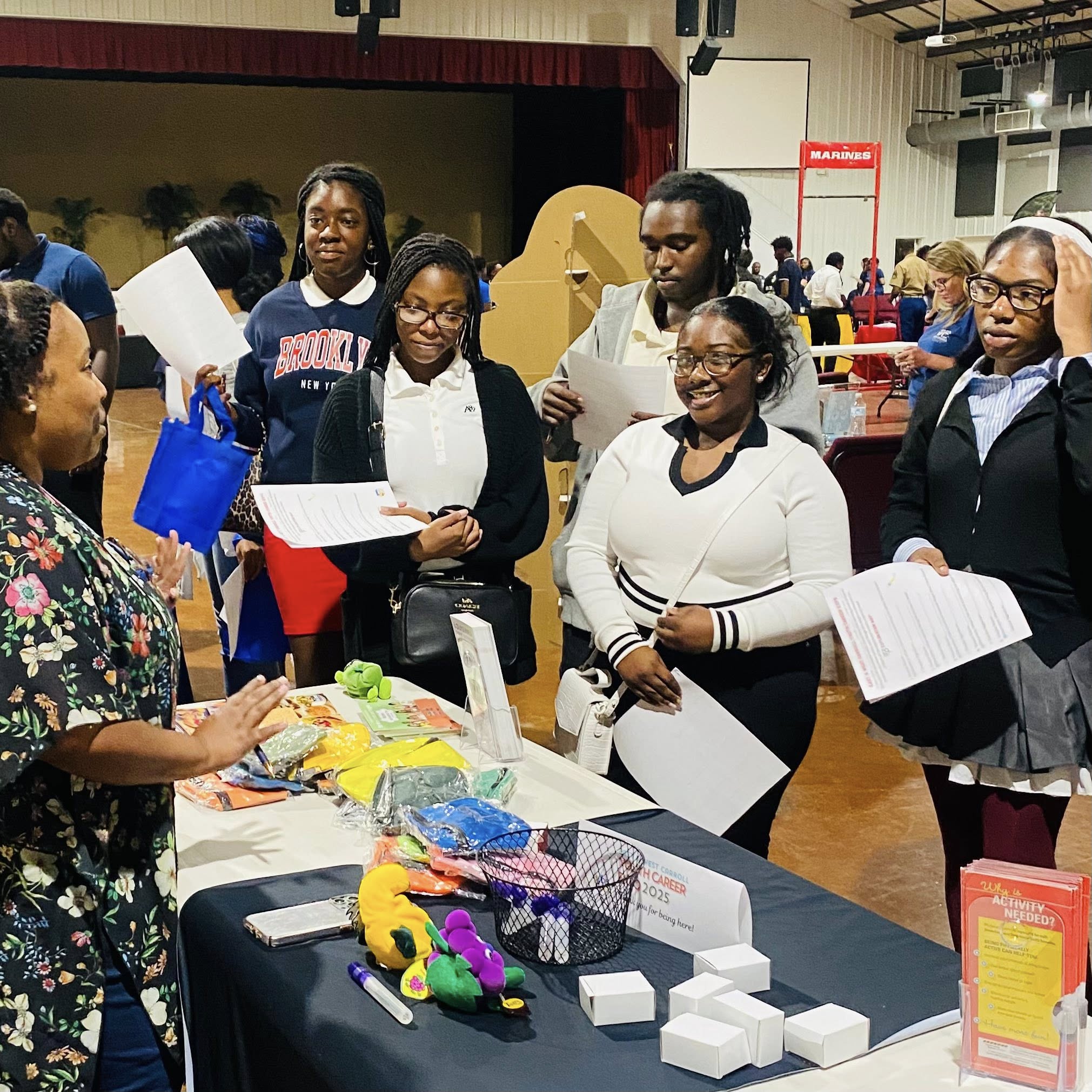 A woman behind a table talking to some teenagers.
